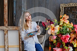 Portrait of a professional artist painting on canvas in the studio. A female artist draws in the workplace. A blonde girl in a
