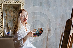 Portrait of a professional artist painting on canvas in the studio. A female artist draws in the workplace. A blonde girl in a