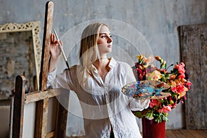 Portrait of a professional artist painting on canvas in the studio. A female artist draws in the workplace. A blonde girl in a