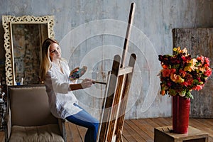 Portrait of a professional artist painting on canvas in the studio. A female artist draws in the workplace. A blonde girl in a