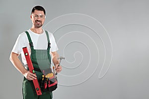 Portrait of professional construction worker with tools on grey background