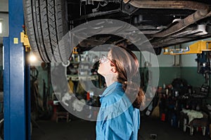 portrait of a professional female auto mechanic working under a vehicle on a lift in service. makes a car inspection