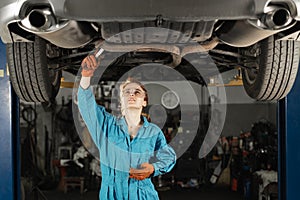portrait of a professional female auto mechanic working under a vehicle on a lift in service. uses a wrench. The