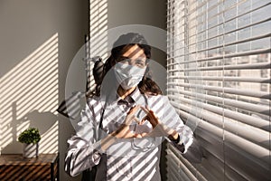 Portrait professional female doctor wearing medical mask showing heart gesture