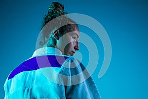 Portrait of professional female judoist isolated on blue studio background in neon light. Healthy lifestyle, sport