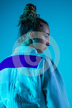 Portrait of professional female judoist isolated on blue studio background in neon light. Healthy lifestyle, sport