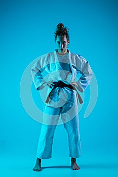 Portrait of professional female judoist isolated on blue studio background in neon light. Healthy lifestyle, sport