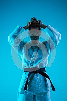 Portrait of professional female judoist isolated on blue studio background in neon light. Healthy lifestyle, sport