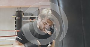 Portrait of professional fighter boxing punching bag in gym. Close-up of young bearded Caucasian man training with