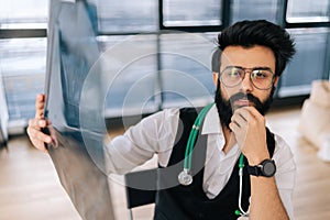 Portrait of professional Indian male doctor in glasses looking at camera with serious expression holding in hand MRI