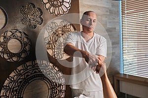 Portrait of professional male masseur massaging heel of foot of unrecognizable female client lying on massage table in