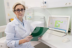 Portrait of professional middle-aged female doctor at work. Serious general practitioner in glasses and lab coat uniform