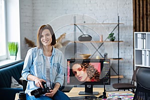 Portrait of professional photographer holding camera in photo studio. Workplace in office with camera, laptop, monitor