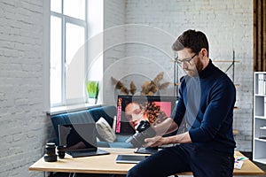 Portrait of professional photographer holding camera in photo studio. Workplace in office with camera, laptop, monitor