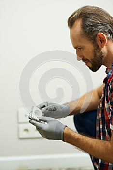 Portrait of professional repairman, electrician wearing protective gloves while installing wall plug socket in a new