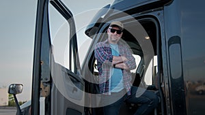 Portrait of Professional Truck Driver sits in his truck and Behind Him Parked Long Haul Semi-Truck.