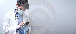 Portrait of professional young male doctor in medical mask and white coat, checking his smartphone