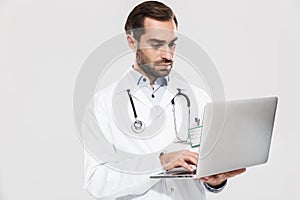 Portrait of professional young medical doctor with stethoscope working in clinic and holding laptop