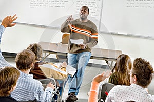 Portrait of Professor pointing at college student with hands raised in classroom