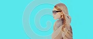 Portrait in profile beautiful young blonde woman looking away wearing coat, sunglasses on blue background