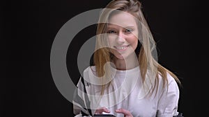 Portrait in profile of young caucasian long-haired girl in white t-shirt typing on smartphone and smiling into camera on