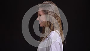 Portrait in profile of young caucasian long-haired girl in white t-shirt watches smilingly into camera on black