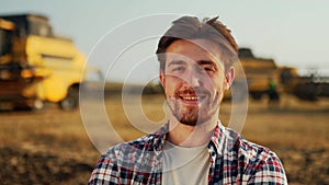 Portrait of proud farmer with hands crossed on chest in harvested wheat field. Harvester machine driver standing at his