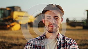 Portrait of proud farmer with hands crossed on chest in harvested wheat field. Harvester machine driver standing at his