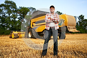 Portrait of proud harvester machine driver with hands crossed on chest. Farmer standing at his combine. Agronomist