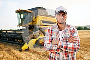 Portrait of proud harvester machine driver with hands crossed on chest. Farmer standing at his combine. Agronomist