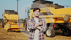 Portrait of proud harvester machine driver with hands crossing on chest. Farmer standing at his combine. Agronomist