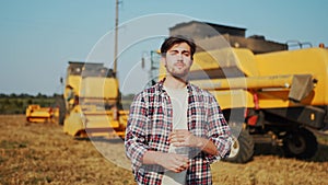 Portrait of proud harvester machine driver with hands crossing on chest. Farmer standing at his combine. Agronomist