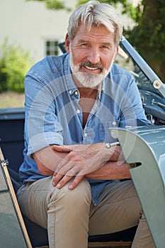Portrait Of Proud Mature Man Sitting In Restored Classic Sports Car Outdoors At Home