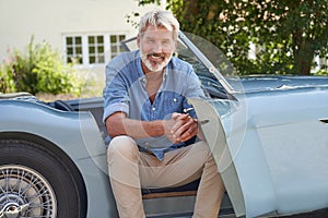 Portrait Of Proud Mature Man Sitting In Restored Classic Sports Car Outdoors At Home