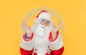 Portrait of a puzzled man in a Santa suit isolated on a yellow background, looking at the camera and confusedly spreads his arms