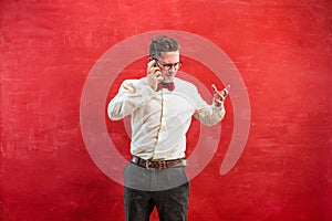 Portrait of puzzled man talking by phone a red background