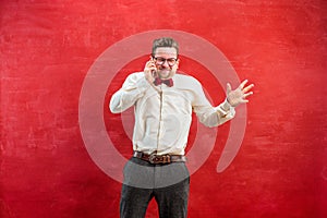 Portrait of puzzled man talking by phone a red background