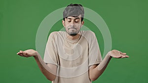 Portrait of puzzled uncertain arabic 20s guy standing on green background unsure embarrassed hispanic man student