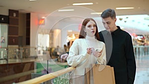 Portrait of puzzled young couple looking for store in shopping mall centre browsing app on mobile phone.