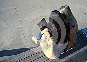 Portrait of real couple of young women, sitting on a bench consulting social networks on their laptop, zenithal view. Concept