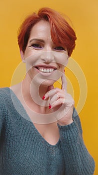 Portrait of red hair woman in her 40s isolated on yellow background.