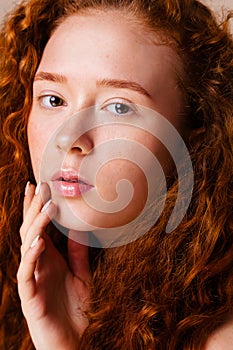 Portrait of red-haired girl with long curly hair and cute freckles on beige background in the studio. Retouched photo. Skin care