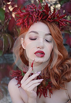 Portrait of a red-haired sexy woman with red full lips in a crown and a necklace of hot chili peppers with a pepper in