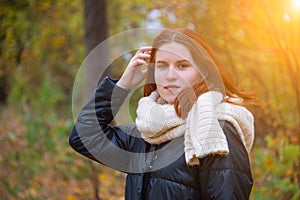 Portrait of a red-haired smiling girl in a jacket and scarf straightening her hair against the background of autumn nature and the