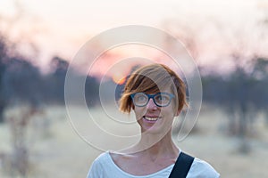 Portrait of a red haired woman with green eyes, eyeglasses and smiling facial expression. Sunset at the horizon. Shot outdoors wit