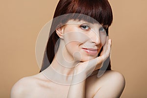 Portrait of red haired woman with natural beautiful skin looking aside over beige studio background