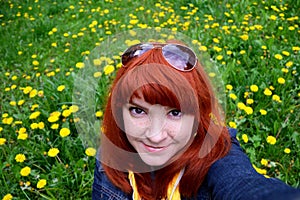 Portrait of a red-haired young woman girl with freckles on a dandelion field