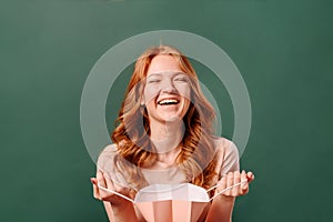 Portrait of a red-headed girl laughing, closing her eyes with a paper bag in her hands