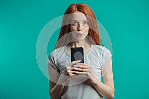Portrait of a redhaired woman holding smartphone over blue background
