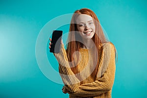 Portrait of a redhaired woman holding smartphone over blue background